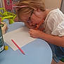 art_supplies, blue_table, child, colorful, creative, drawing, focused, furniture, glasses, headband, indoor, paper, pencil, person, pink, table, toy, white_clothing, writing, young