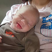 Michael is registered to the contest to win money with this photo: baby, infant, smiling, tongue_out, closed_eyes, person, adult, clothing, shirt, pink, brown_outfit, happy, cute, face, skin, hair, portrait, candid, indoor, holding
