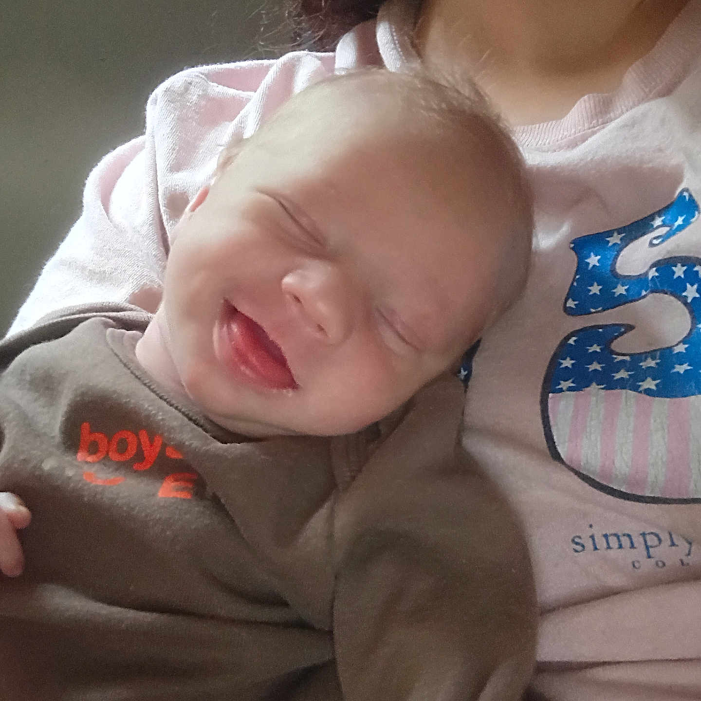 Michael is registered to the contest to win money with this photo: baby, infant, smiling, tongue_out, closed_eyes, person, adult, clothing, shirt, pink, brown_outfit, happy, cute, face, skin, hair, portrait, candid, indoor, holding