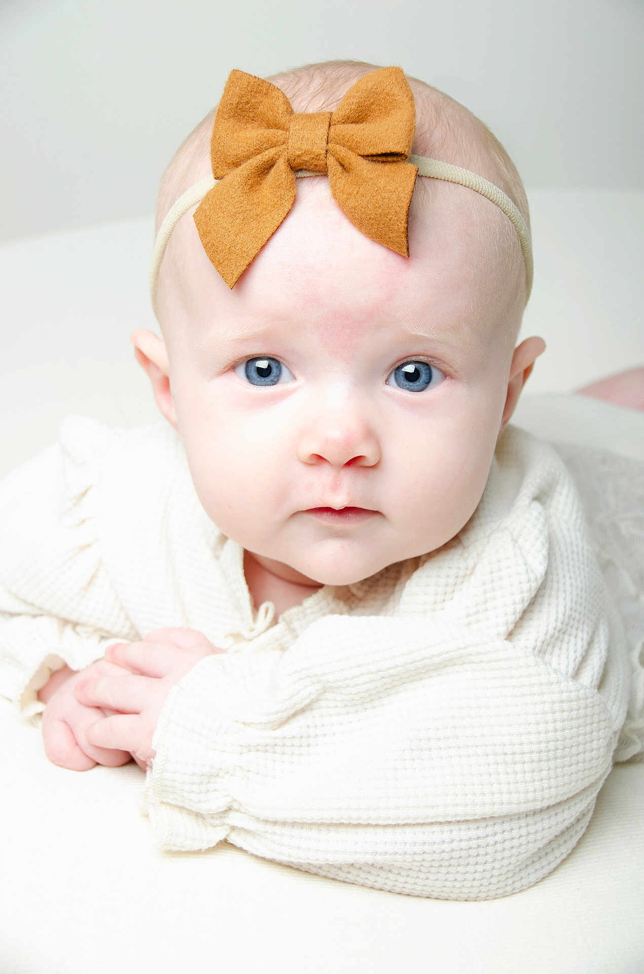 Delilah is registered to the contest to win money with this photo: baby, infant, blue_eyes, headband, bow, white_clothing, close_up, portrait, cute, child, soft_lighting, texture, hands, skin, face, lying_down, innocent, expression, head, person