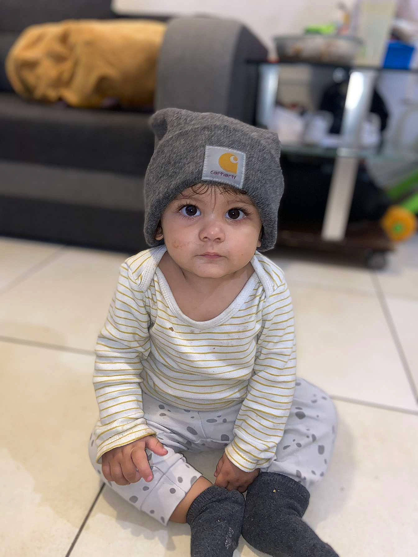 Kélya participe au concours pour gagner de l'argent avec cette photo : baby, baby_toddler_clothing, beanie, cap, cheek, child, comfort, face, fashion_accessory, floor, flooring, fur, headwear, knit_cap, pattern, person, sitting, skin, sleeve, toddler