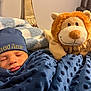 baby, sleeping, blanket, blue, cap, embroidered_text, plush_toy, lion, soft_toy, couch, cozy, indoor, child, face, headwear, comfort, home, rest, cute, toddler