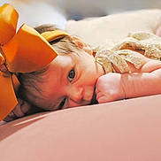 Willow joined the competition — help win amazing prizes! baby, infant, bow, headband, floral_clothing, lying_down, pillow, soft_surface, cute, closeup, face, hand, skin, indoors, portrait, newborn, child, resting, cozy, pink_background