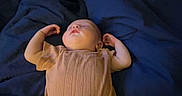 Sophie joined the competition — help win amazing prizes! baby, infant, sleeping, lying_down, bed, blanket, blue_bedding, onesie, ribbed_clothing, arms_raised, face, portrait, indoors, bedroom, dim_lighting, cozy, peaceful, cute, newborn, photography