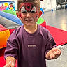 child, smiling, face_paint, spider, portrait, indoor, birthday_party, balloons, inflatables, play_area, purple_shirt, short_hair, standing, hands, fun, colorful, chairs, floor, happy, photography