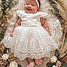 Nohara is registered to the contest to win money with this photo: baby, infant, child, smiling, portrait, white_dress, lace_dress, flower_headband, pink_socks, floral_arrangement, roses, eucalyptus, dried_flowers, dried_grass, blanket, lying_down, indoor, newborn_photography, decorative, happy
