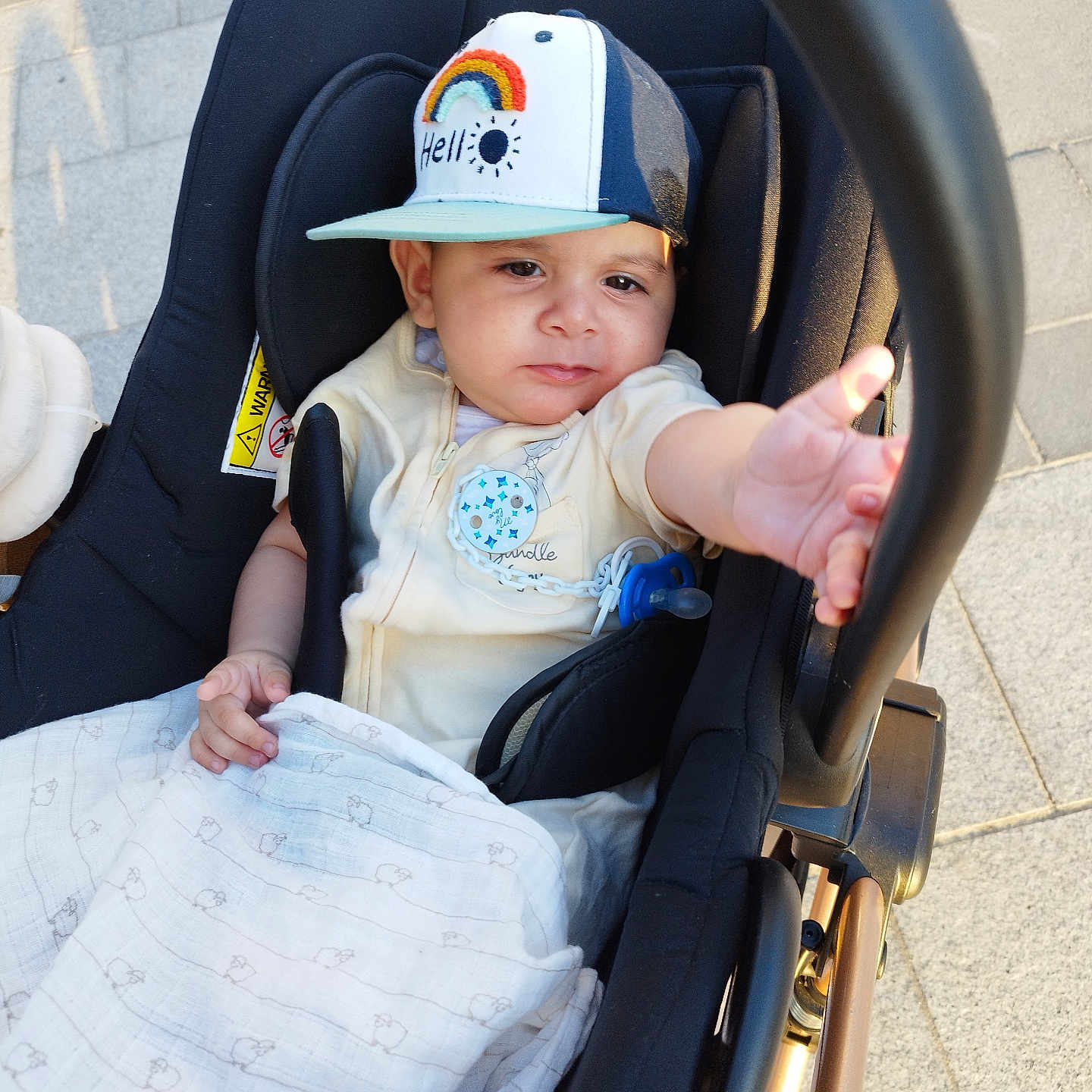 Aryane a rejoint le concours — aidez-le/la à gagner de superbes lots ! baby, blanket, cap, casual, child, clothing, comfort, curious, cute, hand, infant, outdoor, pavement, person, reaching, seat, stroller, sunlight, transport, young