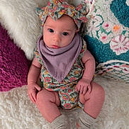 Elliana is registered to the contest to win money with this photo: baby, infant, child, floral_clothing, headband, purple_bib, socks, blanket, pillow, patterned_pillow, cozy, soft_texture, seated, looking_at_camera, indoors, cute, adorable, portrait, colorful, comfortable
