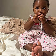 Lyric joined the competition — help win amazing prizes! baby, child, infant, pink_dress, hello_kitty, bed, blanket, indoor, person, cute, toes, hands, face, expression, curious, sitting, soft_lighting, cozy, young, chewing