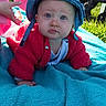 baby, blanket, blue_hat, bright_colors, child, clothing, curious, face, grass, hand, infant, nature, outdoor, person, playtime, portrait, red_jacket, stroller, sunlight, toddler