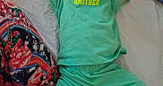 Christopher is registered to the contest to win money with this photo: baby, child, smile, green_clothing, shorts, tshirt, bed, bedding, patterned_fabric, happy, arms_up, lying_down, infant, person, indoors, cute, joyful, face, young_child, playful