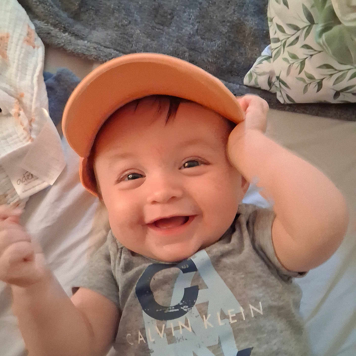 Christopher joined the competition — help win amazing prizes! baby, infant, smiling, cap, hat, calvin_klein, tshirt, clothing, bed, blanket, pillow, happy, cute, child, face, person, indoor, portrait, skin, young
