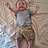 Christopher is registered to the contest to win money with this photo: baby, child, infant, smiling, lying_down, clothing, tshirt, shorts, bed, blanket, plaque, wooden, happy, person, skin, foot, hand, face, indoors, casual