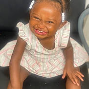 Dionasia is registered to the contest to win money with this photo: toddler, child, smiling, braids, beads, striped_dress, sitting, black_chair, happy, cute, portrait, indoors, skin, hair, young_child, person, face, laughing, baby, fun