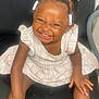 toddler, child, smiling, braids, beads, striped_dress, sitting, black_chair, happy, cute, portrait, indoors, skin, hair, young_child, person, face, laughing, baby, fun