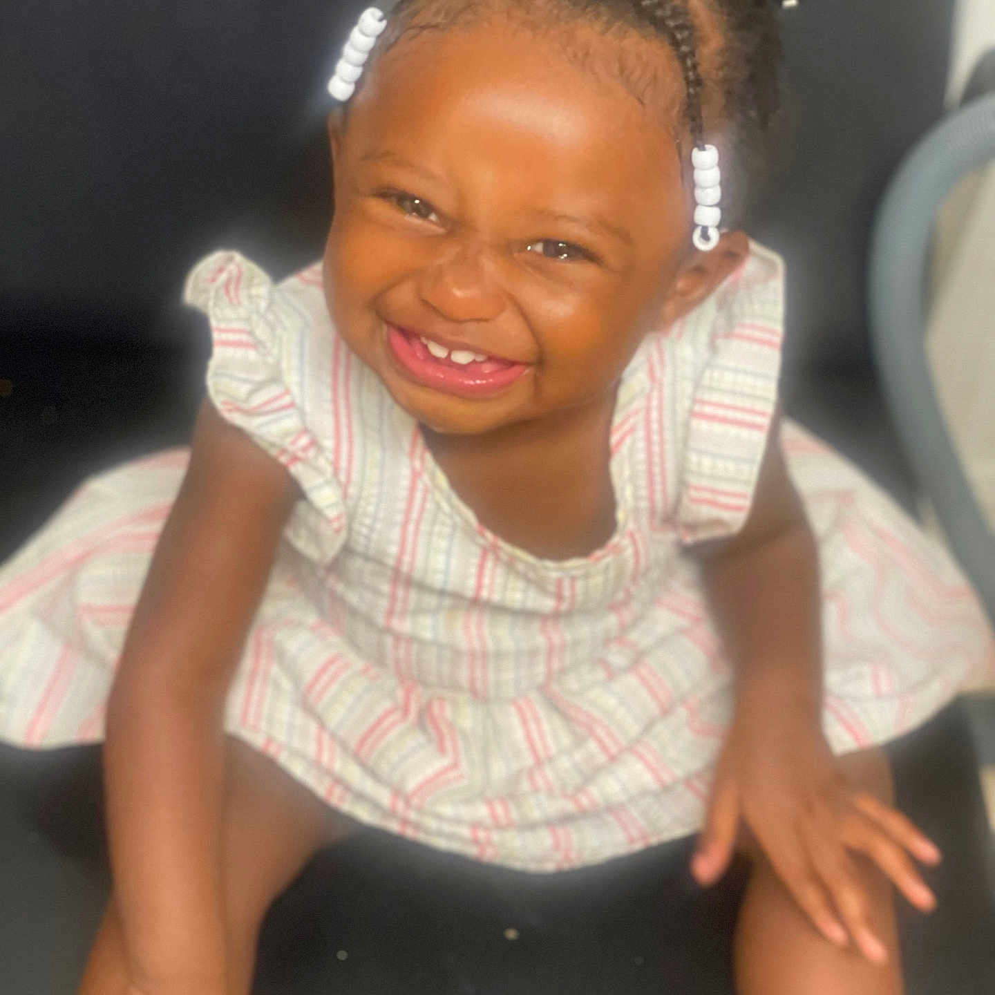 Dionasia is registered to the contest to win money with this photo: baby, beads, black_chair, braids, child, cute, face, fun, hair, happy, indoors, laughing, person, portrait, sitting, skin, smiling, striped_dress, toddler, young_child