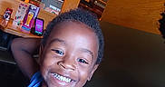 Lamont is registered to the contest to win money with this photo: child, smiling, portrait, indoor, restaurant, happy, boy, casual, blue_shirt, face, hair, furniture, table, television, wood, arm, skin, eyes, mouth, light