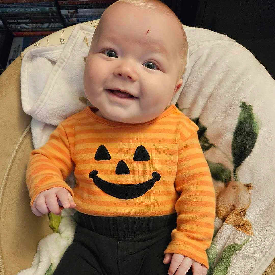 Elijah joined the competition — help win amazing prizes! baby, babylaughing, clothing, coat, cushion, face, furniture, happy, head, homedecor, jacket, knitwear, pants, person, photography, portrait, quilt, sitting, smile, t_shirt