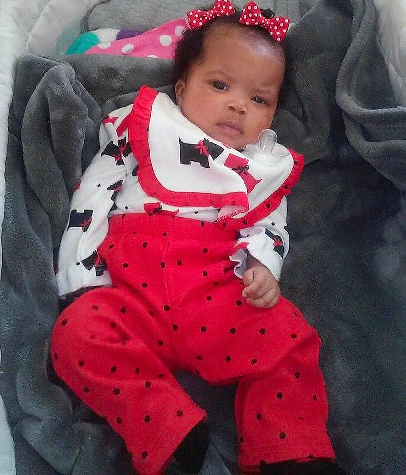 Katelynn is registered to the contest to win money with this photo: arm, baby, baby_products, baby_toddler_clothing, carmine, child, collar, comfort, head, linens, outerwear, pattern, person, pink, red, sitting, sleeve, t_shirt, textile, thigh