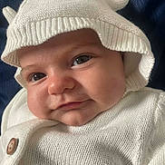 Makinsey is registered to the contest to win money with this photo: baby, infant, face, hat, knitwear, white_clothing, cute, smile, close_up, child, portrait, baby_face, warm_clothing, button, headwear, soft_texture, indoors, blue_background, eyes, cheeks