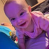 Skylar is registered to the contest to win money with this photo: baby, bed, bedroom, blue_blanket, child, closeup, crawling, face, happy, home, indoors, infant, onesie, photography, pink_clothing, portrait, purple_lighting, sitting, smiling, toy