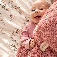 Alora Grace is registered to the contest to win money with this photo: baby, child, smile, blanket, pink, fluffy, bed, floral_pattern, cute, happy, infant, person, clothing, hand, face, portrait, soft_texture, cozy, lying_down, indoors
