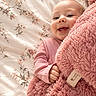 baby, child, smile, blanket, pink, fluffy, bed, floral_pattern, cute, happy, infant, person, clothing, hand, face, portrait, soft_texture, cozy, lying_down, indoors