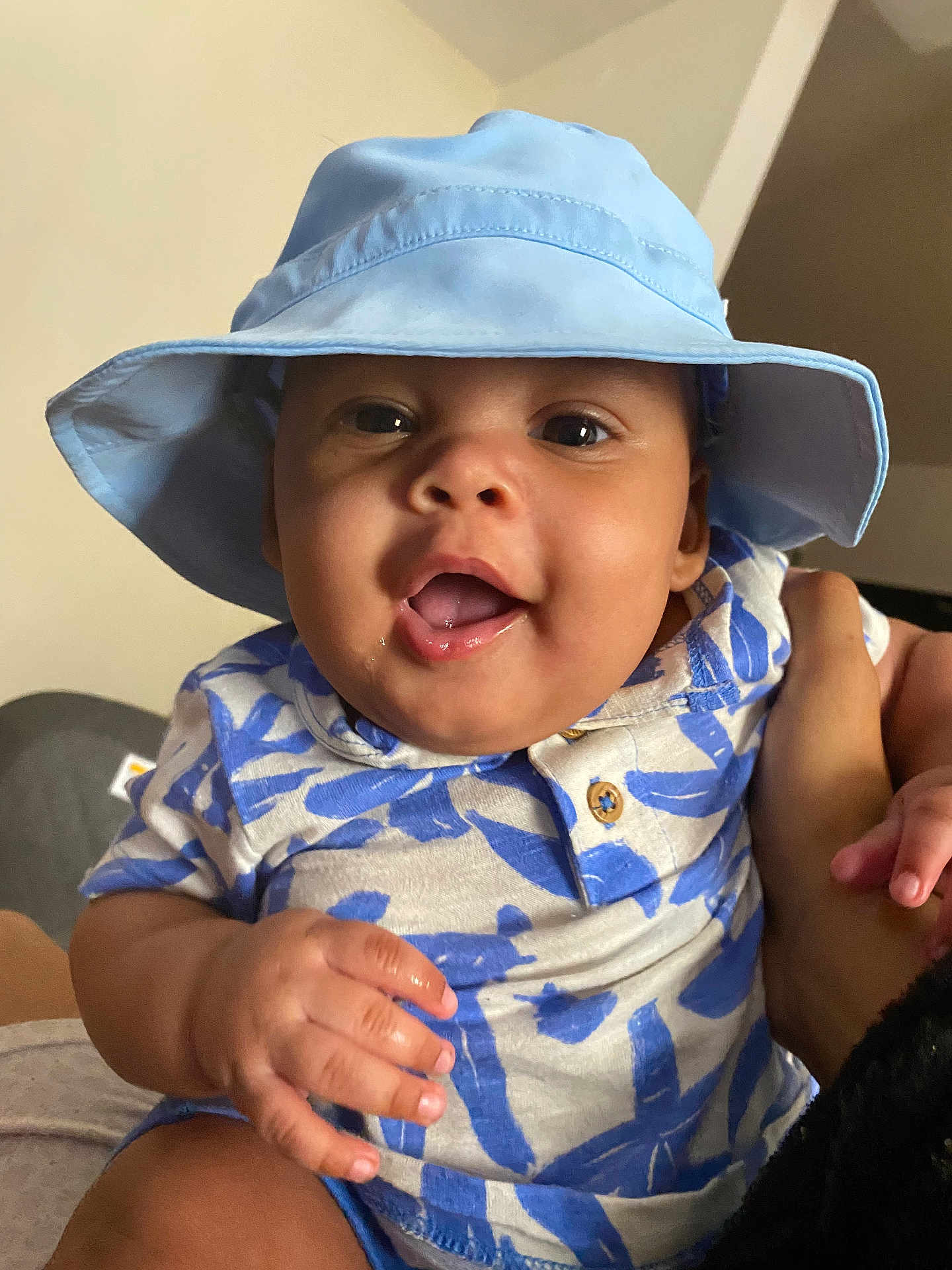 Aramis is registered to the contest to win money with this photo: baby, child, smiling, hat, blue_hat, patterned_shirt, hand, indoor, portrait, happy, person, infant, clothing, cute, face, skin, sitting, holding, expression, young