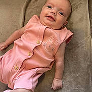 Millie-Mae is registered to the contest to win money with this photo: baby, infant, smile, pink_outfit, bunny_design, cushion, soft_texture, button_shoes, lying_down, cute, child, portrait, indoor, happy, person, young_child, skin, head, face, small_hand