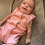 baby, infant, smile, pink_outfit, bunny_design, cushion, soft_texture, button_shoes, lying_down, cute, child, portrait, indoor, happy, person, young_child, skin, head, face, small_hand