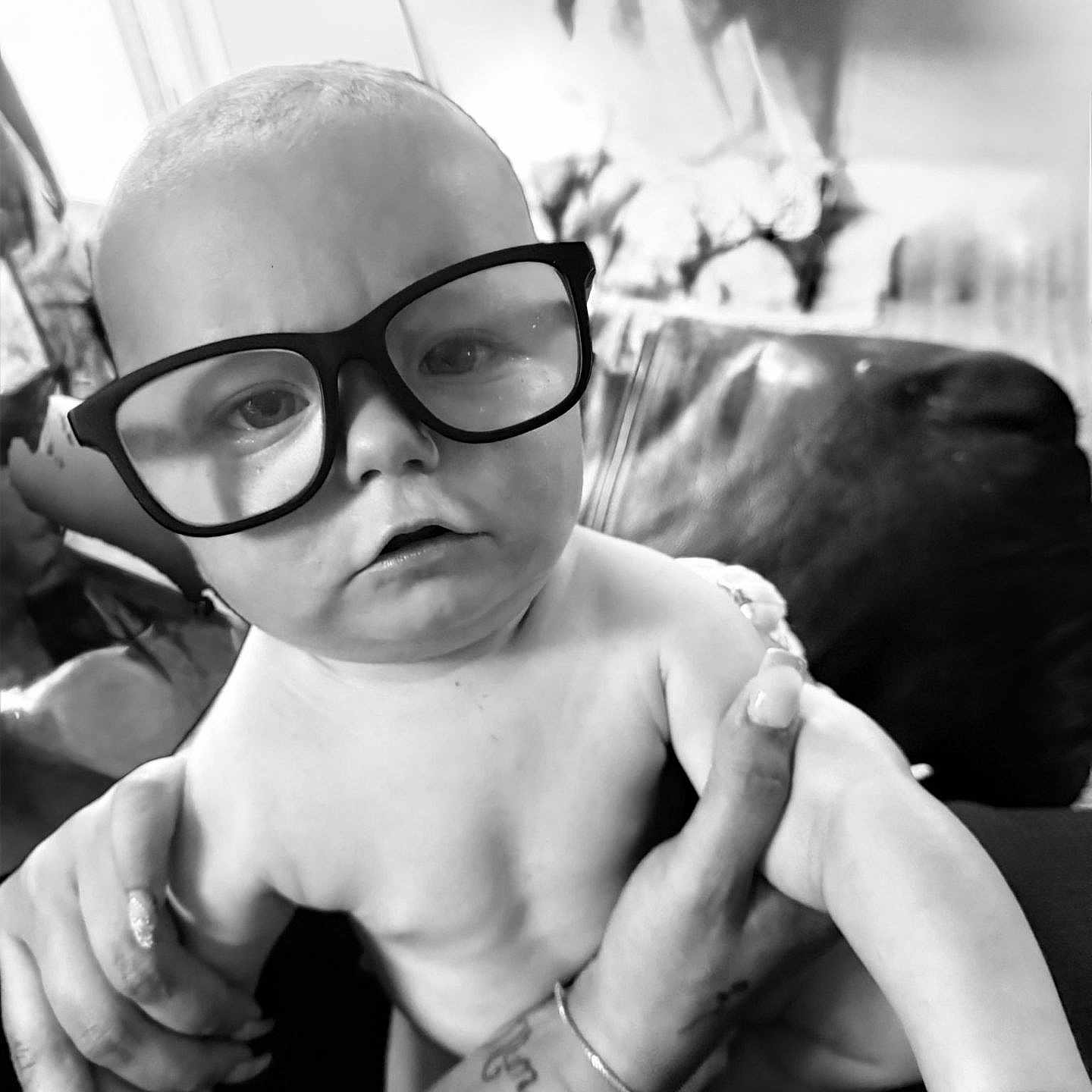 Malakye is registered to the contest to win money with this photo: arm, baby, black_and_white, child, closeup, couch, cute, expression, face, furniture, glasses, hand, holding, indoor, living_room, nail_polish, person, portrait, skin, tattoo