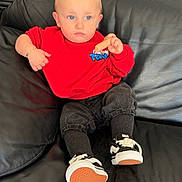 Knay Kraemer a rejoint le concours — aidez-le/la à gagner de superbes lots ! toddler, child, red_sweatshirt, black_pants, sneakers, black_leather_couch, snack, indoor, person, seated, blue_eyes, short_hair, casual_clothing, bracelet, table, chair, floor, background_person, home, relaxed