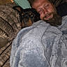 Titan joined the competition — help win amazing prizes! man, dog, blanket, couch, indoor, snuggling, beard, closed_eyes, relaxation, comfort, furniture, pillow, pet, cozy, resting, brown_hair, dark_hair, fur, sleeping, living_room