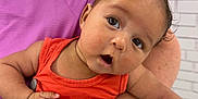 Malakai is registered to the contest to win money with this photo: baby, infant, child, person, holding, orange_clothing, purple_clothing, arm, watch, indoor, store, people, blurred_background, curious, expression, head_tilt, skin, face, eyes, mouth
