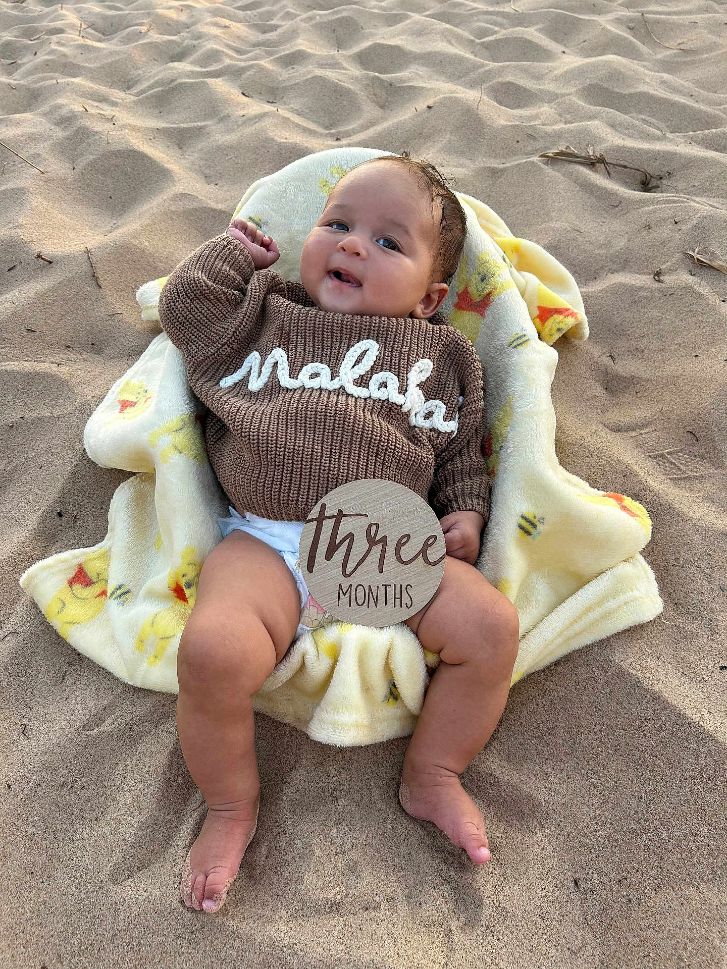 Malakai is registered to the contest to win money with this photo: baby, blanket, brown, child, cute, diaper, face, feet, happy, infant, legs, outdoor, portrait, relaxed, sand, smiling, sweater, three_months, warm_clothing, yellow