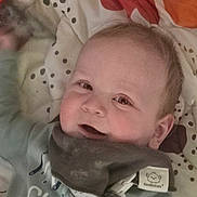 Ezra joined the competition — help win amazing prizes! baby, infant, child, smile, cheeks, eyes, face, bib, blanket, polka_dot, clothing, head, ear, mouth, lying_down, bed, cute, adorable, portrait, home