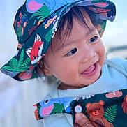 Ryler Isidore is registered to the contest to win money with this photo: baby, child, infant, smiling, happy, portrait, face, eyes, mouth, hat, bucket_hat, animal_print, colorful, clothing, sleeve, hand, indoors, close_up, photography, joyful