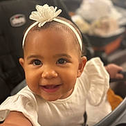 Shyloh is registered to the contest to win money with this photo: toddler, smiling, child, headband, flower, white_clothing, stroller, baby, happy, cute, portrait, face, eyes, skin, infant, young_child, indoor, person, closeup, seat