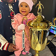 Shyloh joined the competition — help win amazing prizes! baby, child, trophy, pink_clothing, hat, smiling, adult, indoor, table, computer_keyboard, computer_mouse, desktop, sock, mitten, pacifier, person, happy, award, celebration, cute