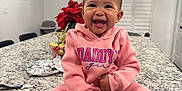 Shyloh is registered to the contest to win money with this photo: baby, child, smiling, hoodie, pink_clothing, sitting, kitchen, countertop, granite, indoor, holiday_decor, poinsettia, lights, happy, cute, person, infant, feet, tableware, modern
