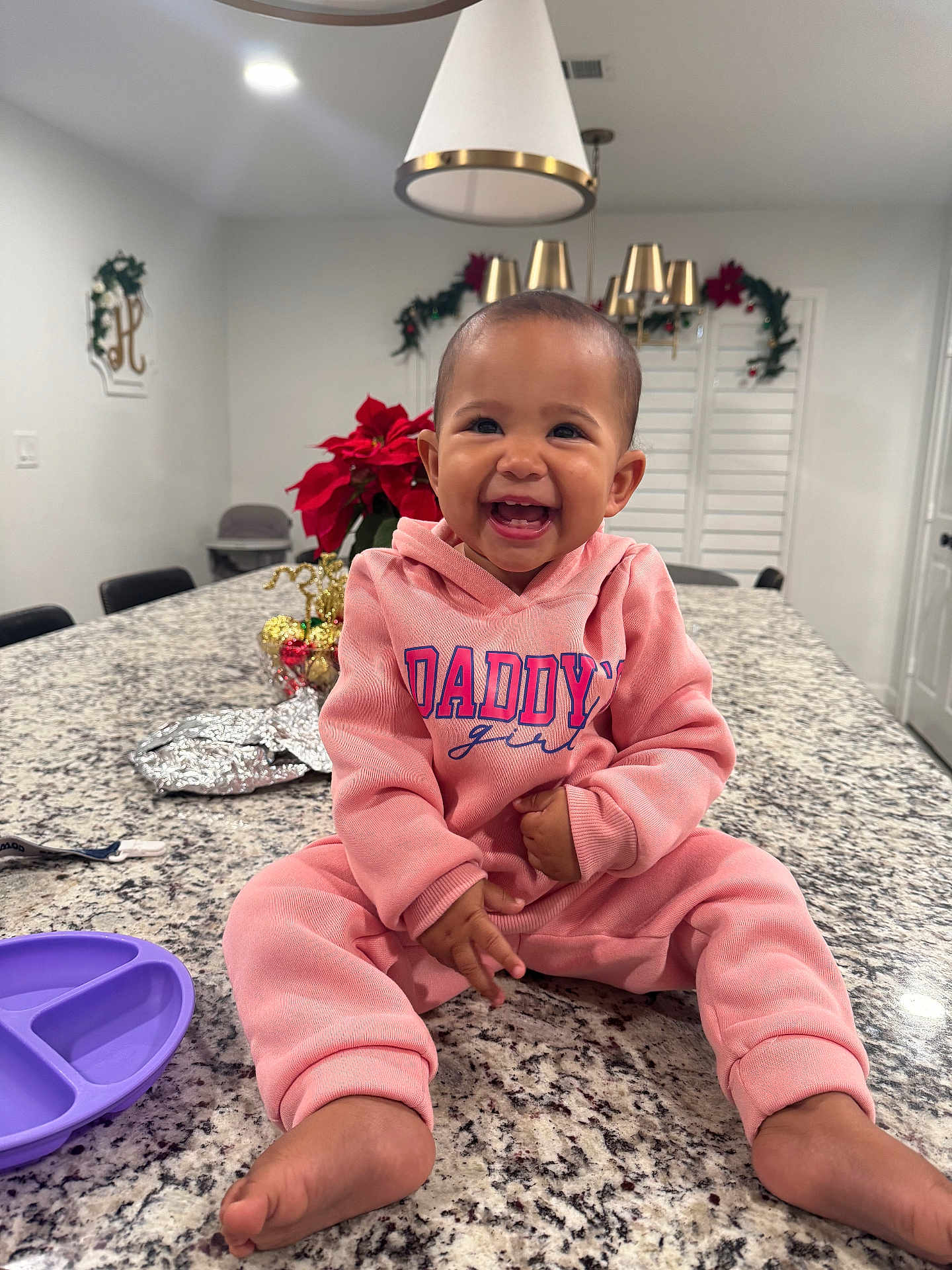 Shyloh is registered to the contest to win money with this photo: baby, child, smiling, hoodie, pink_clothing, sitting, kitchen, countertop, granite, indoor, holiday_decor, poinsettia, lights, happy, cute, person, infant, feet, tableware, modern