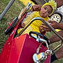 baby, child, yellow_dress, headband, flower, toy_car, fire_truck, grass, outdoor, hands, car, wheel, red, black_car, summer, play, vehicle, person, support, sunlight