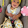 baby, child, car_seat, yellow_headband, flower, smiling, happy, toy_giraffe, pink_flower_toy, lemon_pattern, clothing, socks, cute, infant, seatbelt, indoors, portrait, closeup, playful, comfortable