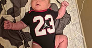 Sion joined the competition — help win amazing prizes! baby, infant, child, portrait, lying_down, bed, bedding, blanket, basketball_jersey, sportswear, number_23, orange_socks, fist, arms, legs, wide_eyed, indoor, bedroom, patterned_fabric, happy