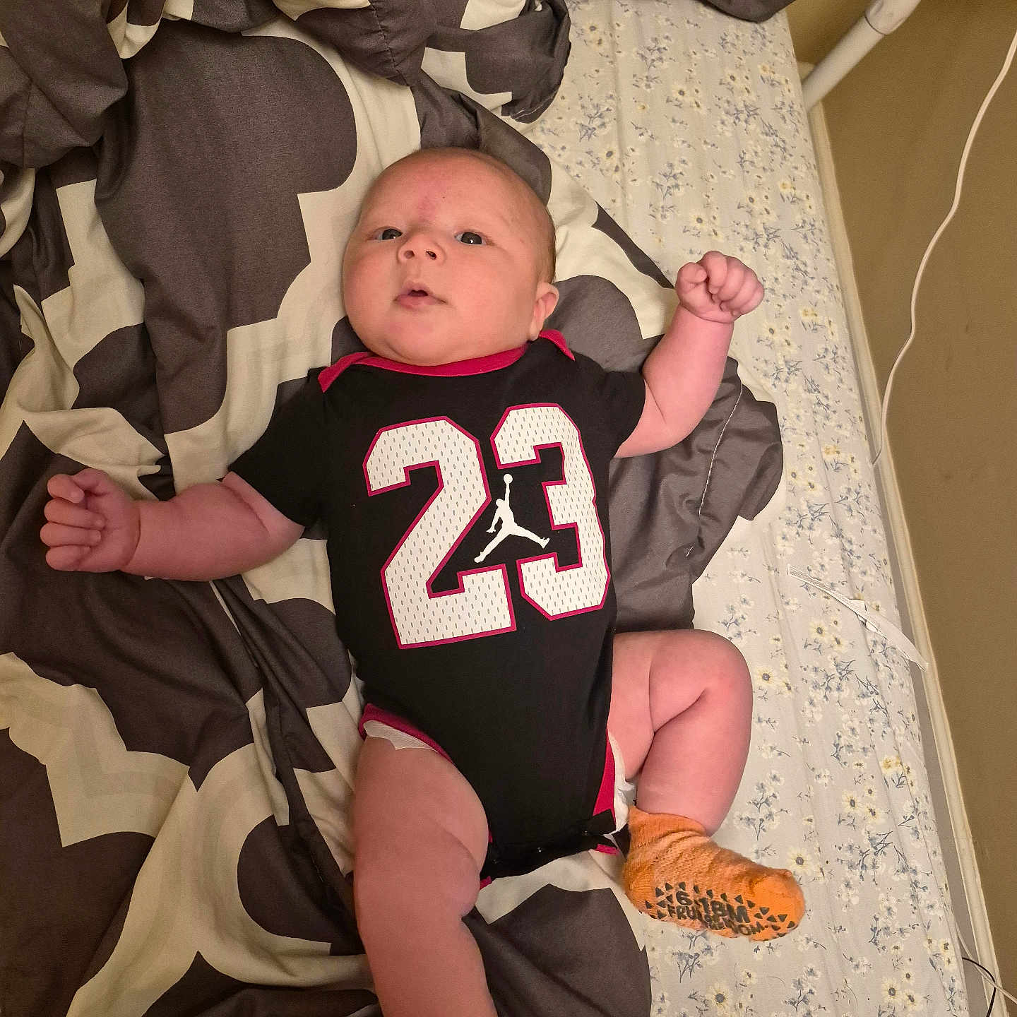 Sion joined the competition — help win amazing prizes! baby, infant, child, portrait, lying_down, bed, bedding, blanket, basketball_jersey, sportswear, number_23, orange_socks, fist, arms, legs, wide_eyed, indoor, bedroom, patterned_fabric, happy