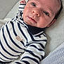 baby, infant, striped_clothing, whale_emblem, lying_down, curious_eyes, face, hand, cozy, cute, child, person, soft_lighting, indoor, portrait, newborn, clothing, fabric, closeup, expression