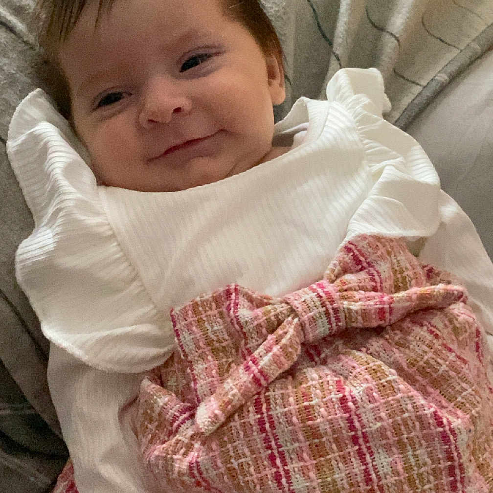 Ayrah joined the competition — help win amazing prizes! baby, blanket, bow, child, couch, cozy, cute, fashion, happy, indoors, infant, person, pink_skirt, portrait, resting, ribbons, smile, soft_lighting, white_clothing, young_child