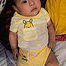 baby, child, infant, portrait, lying_down, sitting, yellow_clothing, striped_shirt, bear_design, bed, bedding, blanket, pillow, face, eyes, looking_at_camera, indoors, cute, eiffel_tower_pattern, photograph