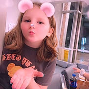 Skylar joined the competition — help win amazing prizes! child, girl, indoor, casual_clothing, hand_gesture, blowing_kiss, filter, pink_ears, pink_nose, long_hair, seated, modern_room, chairs, bottle, beverage, table, window, glass, person, playful_expression