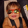 automotive, baby, car_seat, child, close_up, eyes, face, fashion, hair, humorous, indoor, infant, orange_glasses, photograph, portrait, safety, seatbelt, seated, smiling, sunglasses